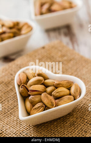 Pistachio nuts in heart shaped ceramic bowls on white wooden background Stock Photo
