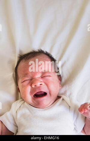 Close up of mixed race baby crying on bed Stock Photo