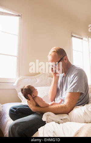 Father talking on cell phone and holding baby on bed Stock Photo