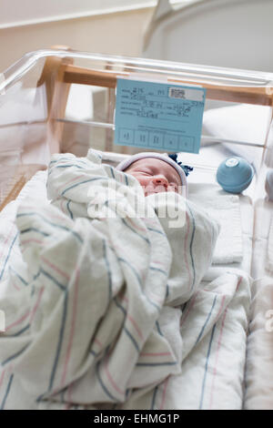 Mixed race wrapped in blanket in hospital crib Stock Photo