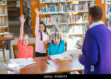 Students raising their hands in library Stock Photo