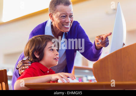 Teacher helping student use computer in library Stock Photo