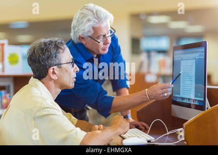 Teacher helping adult student use computer in library Stock Photo