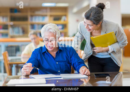 Teacher helping adult student in library Stock Photo