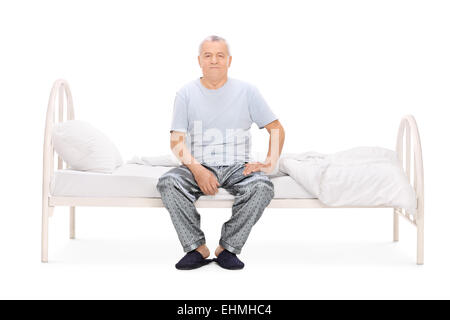 Senior man in pajamas sitting on a bed isolated on white background Stock Photo