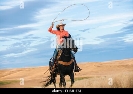 Caucasian woman on horse throwing lasso in grassy field