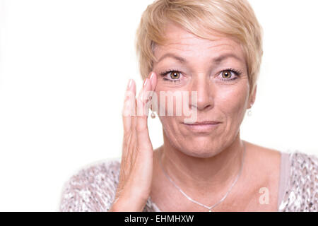 Attractive senior blond woman with a wide-eyed expression and her glasses on her head checking her complexion Stock Photo