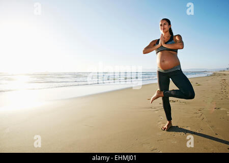 Pregnant Hispanic woman practicing yoga on beach Stock Photo