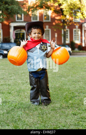 Mixed race boy in cowboy costume holding pumpkin pails on Halloween Stock Photo