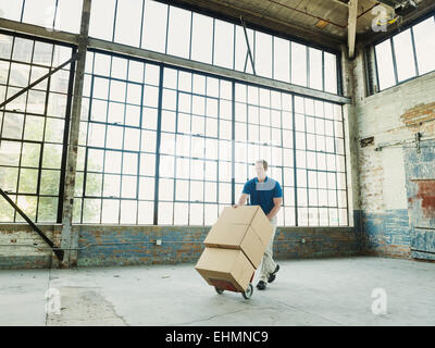 Caucasian businessman pushing cardboard boxes on hand truck in warehouse Stock Photo