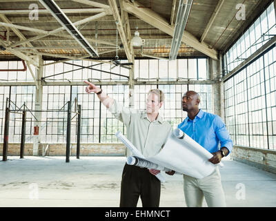 Businessmen reading blueprints in empty warehouse Stock Photo