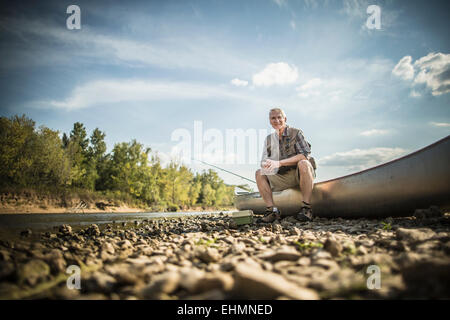 Older Caucasian man sitting in canoe on riverbed Stock Photo