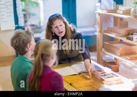 Caucasian Montessori teacher helping students in classroom Stock Photo