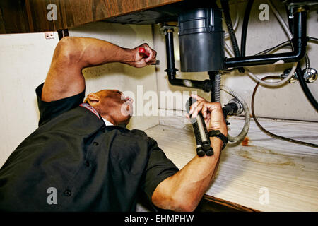 Mixed race plumber working under sink Stock Photo