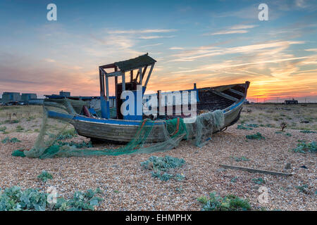 Beautiful dramatic sunset over an old weathered fishing boat with nets on a pebble beach Stock Photo