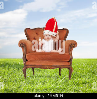 baby in royal hat with lollipop sitting on chair Stock Photo