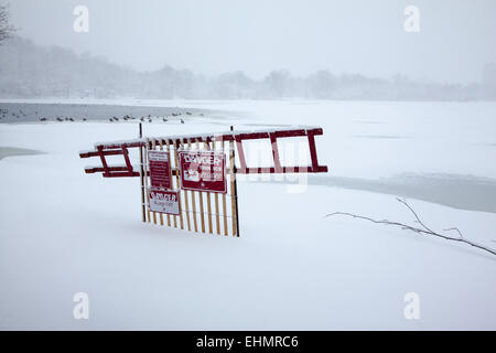 Danger, thin ice sign along the frozen snow covered lake In Prospect Park, Brooklyn New York on a snowy day. Stock Photo