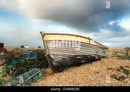 An old wooden fishing boat rests on a shingle beach alongside abandoned lobster pots Stock Photo