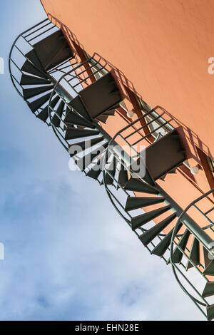 Abstract architecture fragment, old metal spiral ladder on the red wall Stock Photo