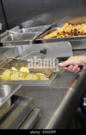 Chef deep frying potatoes in a commercial kitchen in the UK. Stock Photo