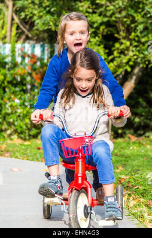 5 and 7 years old girls riding a bicycle. Stock Photo