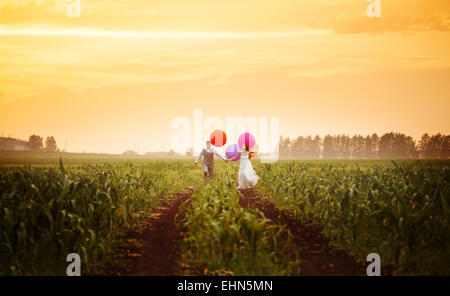 Happy young wedding couple running on the sunset field with big bright colorful balloons Stock Photo