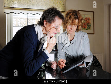 Old age pensioner female and younger woman using an Apple iPad tablet computer at home Stock Photo