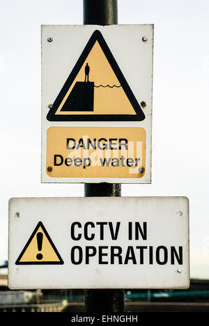 Signs at a harbour warning about deep water, and that CCTV is in operation Stock Photo