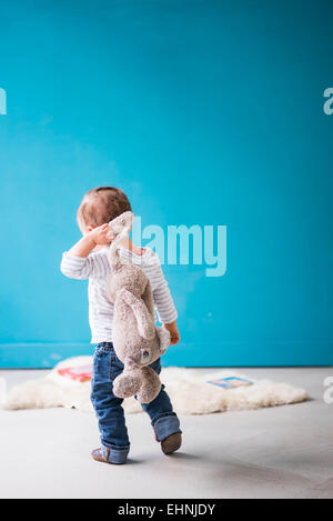 Toddler walking away from camera with rabbit toy over shoulder Stock Photo