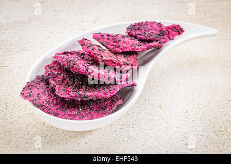 slices of dried red dragon fruit on a teardrop shaped bowl against rustic wood Stock Photo