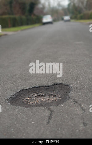 In need of repair a pothole appears in the middle of a tarmacked road surface creating a hole to throw cyclists off accidents Stock Photo