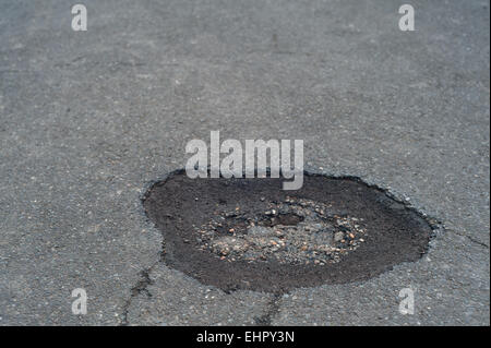 In need of repair a pothole appears in the middle of a tarmacked road surface creating a hole to throw cyclists off accidents Stock Photo