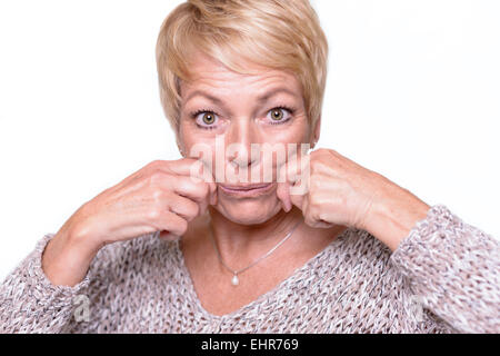 Attractive middle-aged woman with short blond hair trying to reverse the signs of aging by pulling on her cheeks with her hands Stock Photo