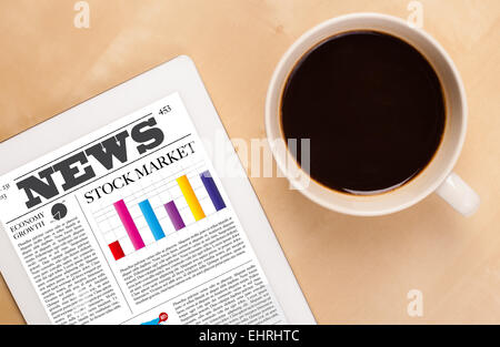 Tablet pc shows news on screen with a cup of coffee on a desk Stock Photo