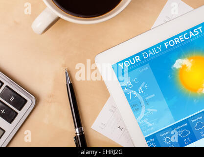 Tablet pc showing weather forecast on screen with a cup of coffee on a desk Stock Photo