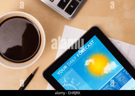 Tablet pc showing weather forecast on screen with a cup of coffee on a desk Stock Photo