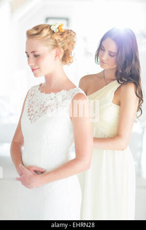 Bridesmaid helping bride with dressing in bedroom Stock Photo