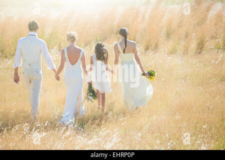 Young couple with bridesmaid and girl walking in meadow Stock Photo