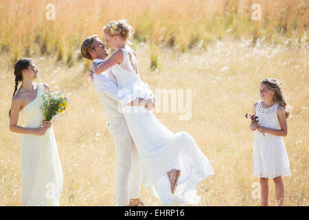 Bridesmaid and bridesmaid watching and laughing,Young couple embracing in meadow Stock Photo