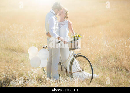 Young couple with bike kissing in meadow Stock Photo