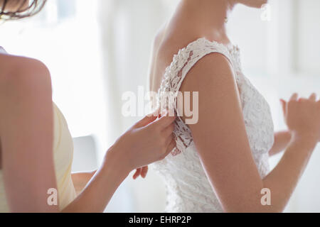Bridesmaid helping bride with dressing in domestic room Stock Photo