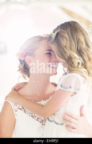 Bride holding bridesmaid in domestic room Stock Photo