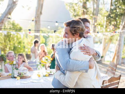Bridegroom and best man embracing during wedding reception in domestic garden