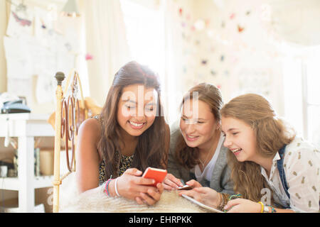 Three teenage girls using smartphone together while lying on bed in bedroom Stock Photo