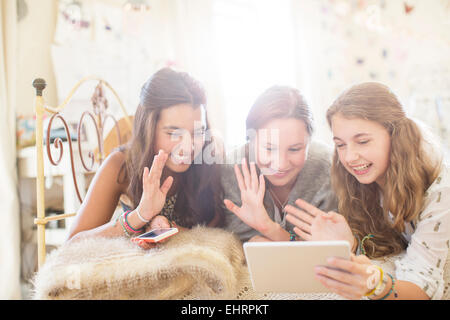 Three teenage girls lying on bed and communicating using digital tablet Stock Photo