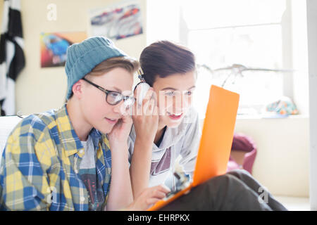 Two teenage boys sharing laptop and headphones in room Stock Photo