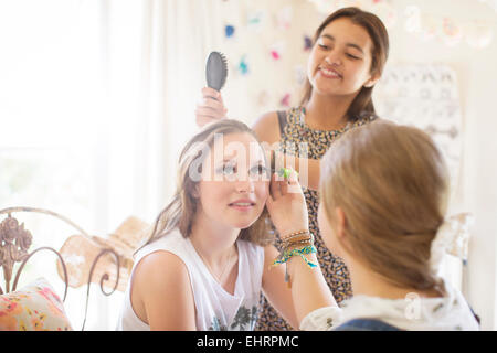 Three teenage girls doing make-up and brushing hair in bedroom Stock Photo