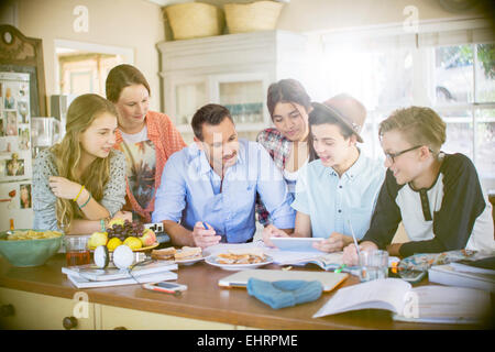 Group of teenagers with mid adult man using digital tablet at table in dining room Stock Photo