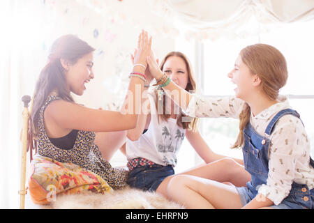 Three teenage girls doing high five on bed Stock Photo