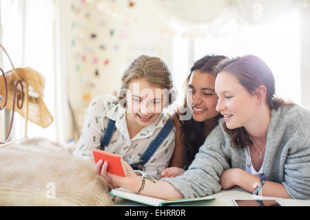 Three teenage girls using smartphone together while lying on bed Stock Photo